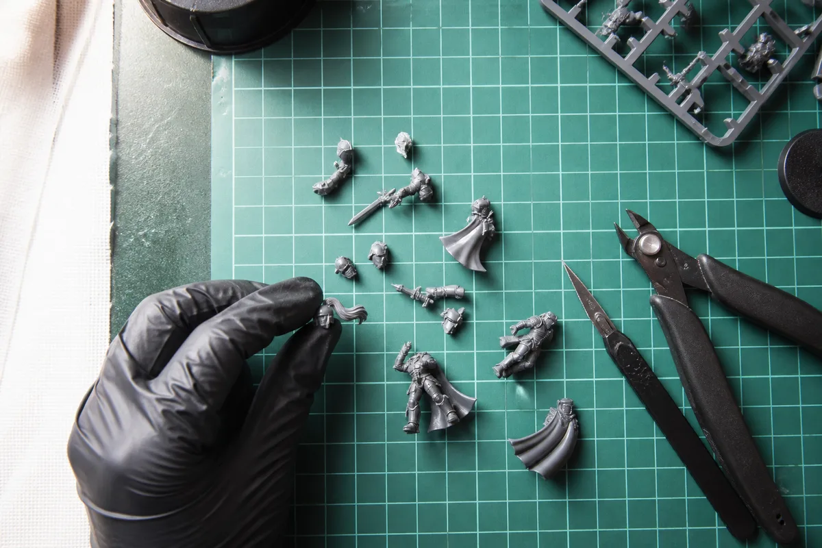 Pièces de figurines détachées de leur grappe posées sur un tapis de découpe avec une pince coupante