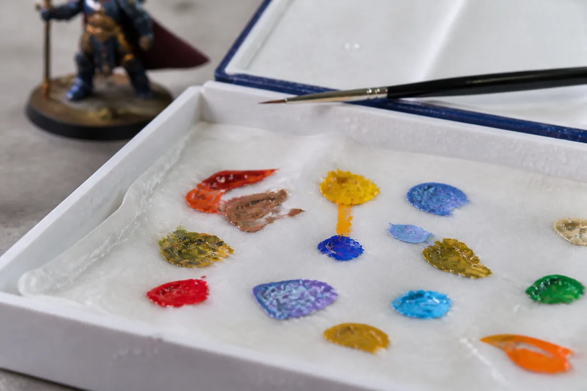 Palette humide ouverte avec des mélanges de peinture acrylique et un pinceau fin posé à côté