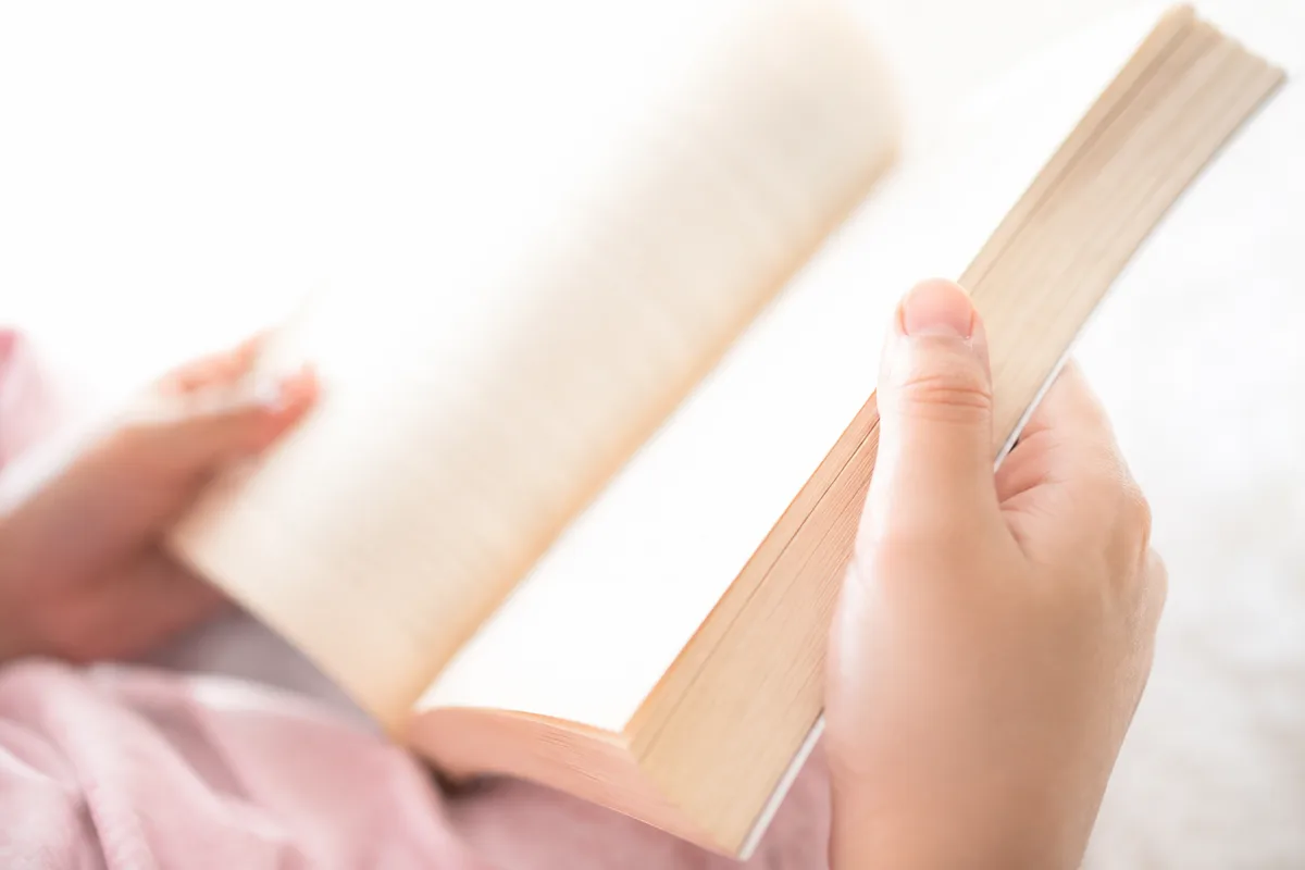 Mains d’enfant tenant un livre ouvert près d’une fenêtre lumineuse
